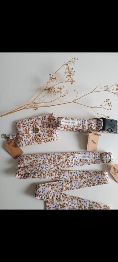 Collares de tela en tonos beige y blanco, con etiquetas de marca, junto a ramas secas.